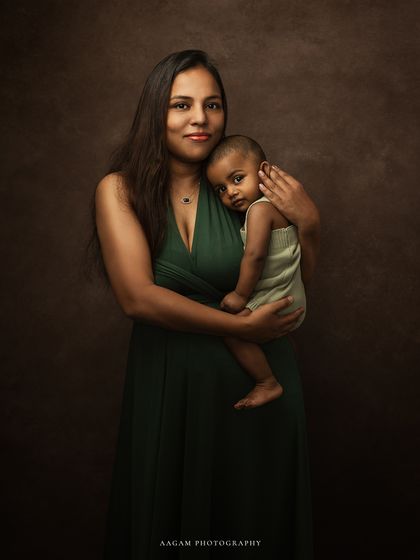 In the softest whispers and gentlest touch. A mother in a beautiful green gown holds her baby close. The rich, dark background creates a painterly feel.