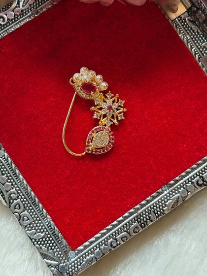 A modern designer nath featuring American diamonds and a red stone drop.