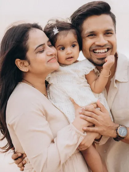 A warm, happy family portrait where a mother and father embrace their baby. The genuine smiles and close connection make this a perfect memory from their seaside family photoshoot.