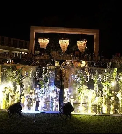 An elegantly designed bar setup for an evening event, beautifully lit and decorated with flowers and chandeliers.
