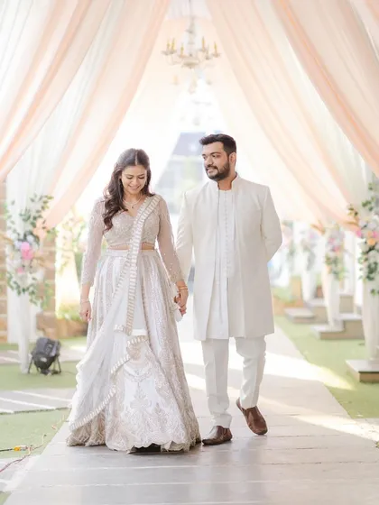 Walking into their future together. This full-length shot showcases how the complete look, from the elegant hairstyle to the flawless makeup, complements the bride's stunning white lehenga.