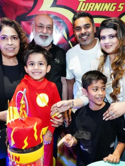 A happy family celebrates a superhero-themed birthday. The birthday boy is dressed as The Flash, ready to enjoy his action-packed party.