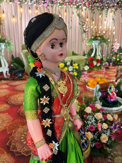 A close-up of a beautiful doll dressed in a traditional green and red saree with intricate jewelry.