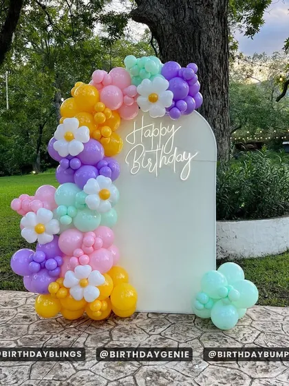 A cheerful and colorful balloon garland on a white arched backdrop. The mix of pastel purple, pink, yellow, and mint, along with daisy-shaped balloons, is perfect for a spring or summer party.