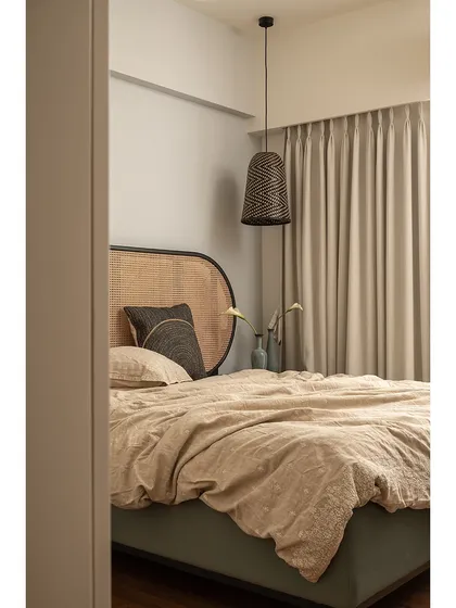 A peek into the guest bedroom, showcasing the beautiful rattan headboard and the soft, rumpled linen bedding. The space is a perfect example of how to create a relaxed yet stylish retreat.