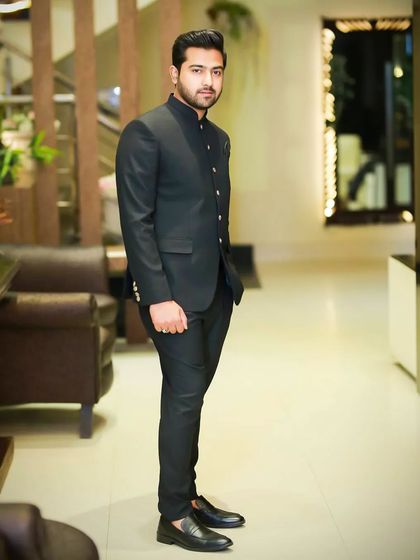 A full-body shot of a client in a black Jodhpuri suit. The grooming is impeccable, creating a sleek and modern silhouette that is perfect for a formal evening event.