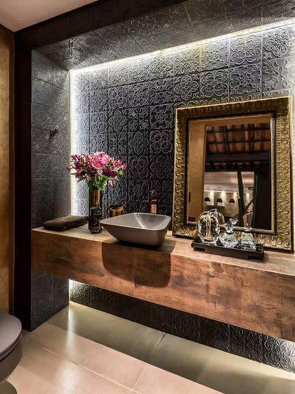 We created a rustic yet elegant powder room with a thick, floating wooden slab as the vanity counter. The design is enhanced by a textured, dark tile backsplash, an ornate gold-framed mirror, and soft under-counter lighting.