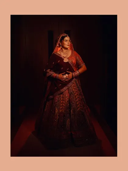 A full-length shot of the bride in her red lehenga, using dramatic, low-key lighting to create a powerful and cinematic bridal portrait.