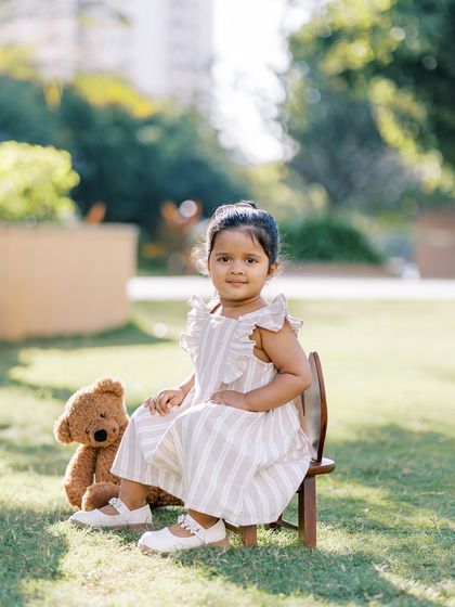 A little girl sitting on a chair with her teddy bear. A sweet and simple portrait in a lovely outdoor setting.