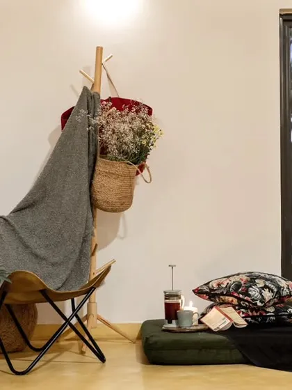A stylishly relaxed corner featuring a leather butterfly chair, a wooden coat rack, and floor cushions. The large glass door in the background connects the space to the outdoors, enhancing its airy feel.