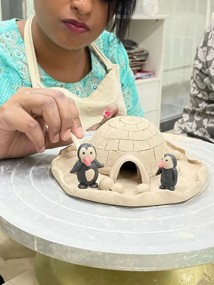 A student adds the finishing touches to a delightful scene featuring an igloo and penguins, all sculpted by hand from clay.