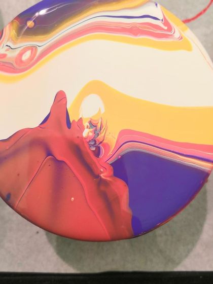 A beautiful pour in progress on a circular coaster, with shades of purple, yellow, and red creating a sunset-like effect.