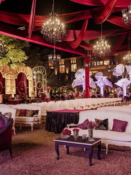 A sweeping view of 'The Scarlet Soirée' for Aashvi and Akash. The venue is bathed in rich red tones, with elegant lounge seating, dramatic draping, and large, illuminated floral trees creating a romantic and opulent atmosphere.