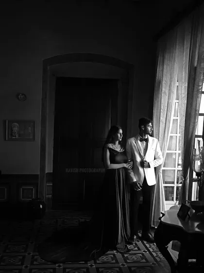 An artistic black and white shot of the couple by a window, using natural light and shadow to create a dramatic, moody portrait.
