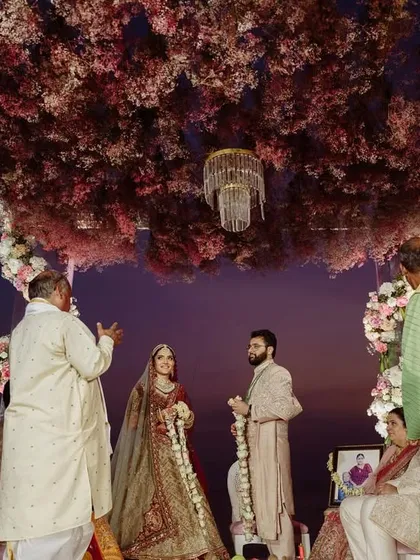 The wedding ceremony set against a beautiful sunset. The mandap, with its ceiling of pink baby's breath, creates a magical atmosphere for the Varmala and pheras.