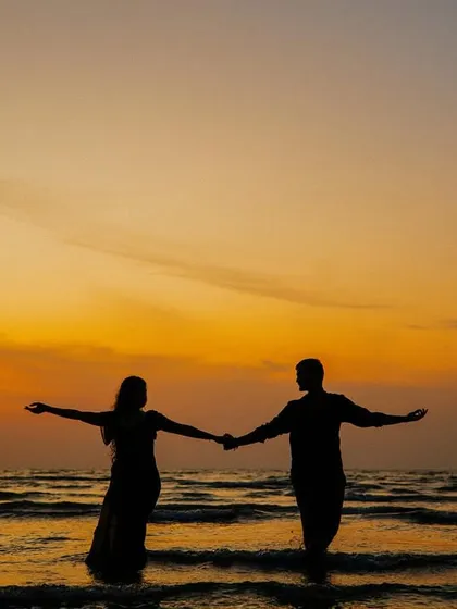 A beautiful silhouette of a couple standing in the water at sunset, their arms outstretched. This serene image captures a moment of peace and togetherness.