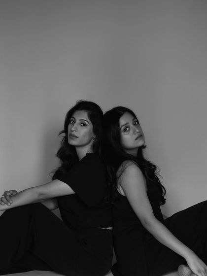 A powerful portrait of two friends seated back to back, looking towards the camera. Their expressions are strong and confident.