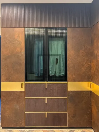 This section of the wardrobe features ribbed glass doors, which offer a glimpse of the clothing inside while maintaining a tidy appearance. Below, the textured drawers and sleek gold handles continue the theme of modern luxury and tactile finishes.