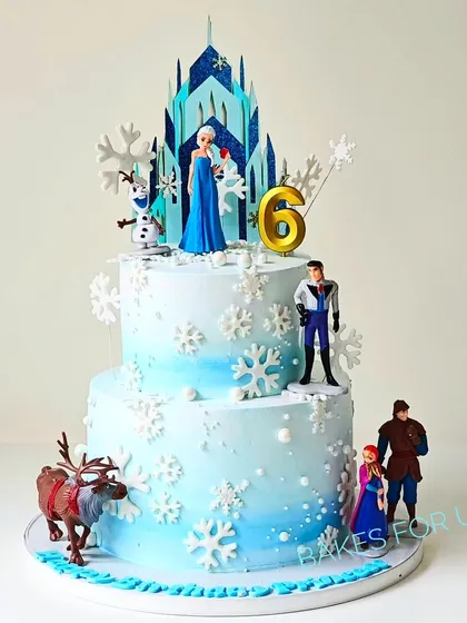 A magical two-tier Frozen-themed cake featuring Elsa, Anna, Olaf, and other characters from the beloved movie. The cake is decorated with shimmering snowflakes and an icy blue ombre effect.