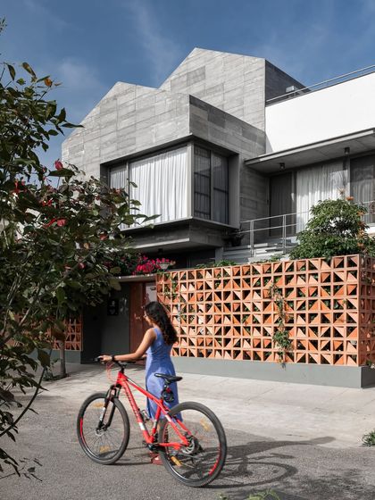 The exterior of 'Roots' showcases a cantilevered volume clad in local stone and a terracotta screen. This combination of textures and forms provides privacy from the street while adding a unique, modern character to the home's facade.