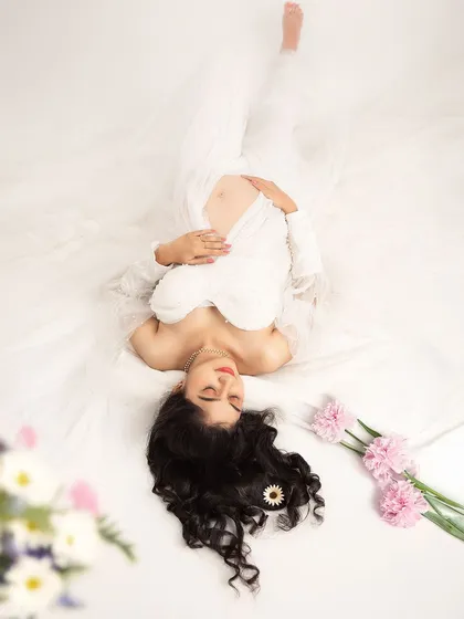 A creative and serene overhead shot. The mother-to-be lies in a bed of white, creating a peaceful and angelic composition.