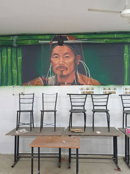 This image shows the tribal man portrait mural in its final setting within a university classroom. The artwork is framed by a painted bamboo motif, connecting the subject to traditional handicrafts and materials.