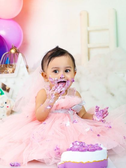 A princess in pink enjoying her purple cake. The contrast of colors and her joyful, messy expression make this an absolutely adorable cake smash photo.