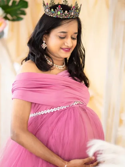 A soft and delicate portrait. The mom-to-be, wearing a pink gown and crown, looks down at her bump with a gentle smile, capturing the tender emotions of pregnancy.