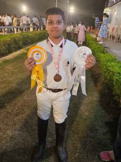 A young rider proudly displays his ribbons and medal. Every achievement, big or small, is a huge confidence booster.
