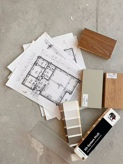 On-site decisions are crucial. Here, architectural drawings are laid out on the concrete floor alongside wood samples and paint swatches to finalize the material palette.