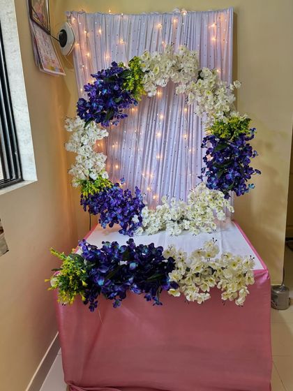A modern floral ring design using clusters of purple and white orchids. Set against a white curtain with fairy lights, this setup is both contemporary and beautiful.