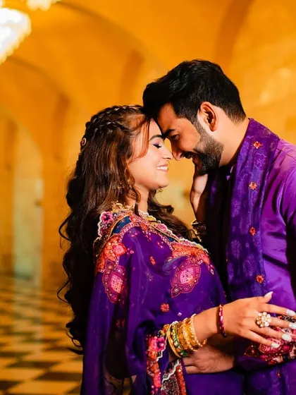 A romantic shot of a couple, where the bride's hair is styled in a half-up braid with soft curls, perfectly matching the vibrant purple of her outfit.