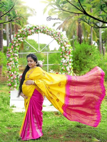 A graceful solo portrait of a mother-to-be in a yellow and pink saree, with the fabric flowing beautifully.