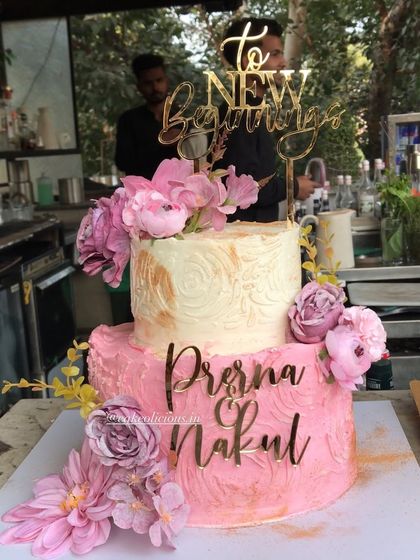 A pretty two-tier engagement cake for a new beginning. The bottom tier has a pink textured finish, while the top is a classic white with gold stenciling, all brought together with beautiful pink flowers and custom name toppers. The flavor was a crowd-pleasing white forest.