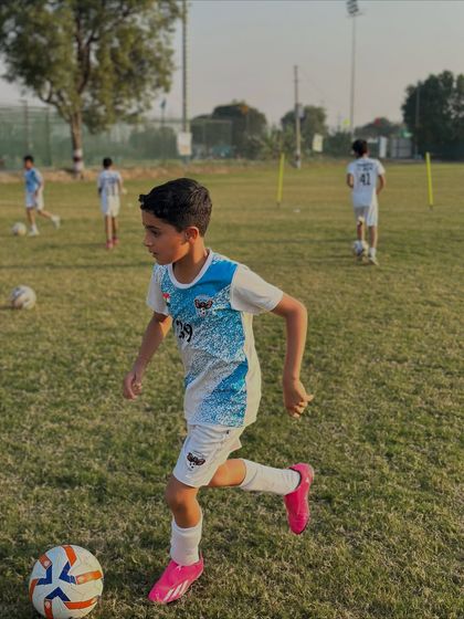 A young player in mid-stride, dribbling the ball during a training exercise. We focus on developing strong fundamental skills like this from day one.