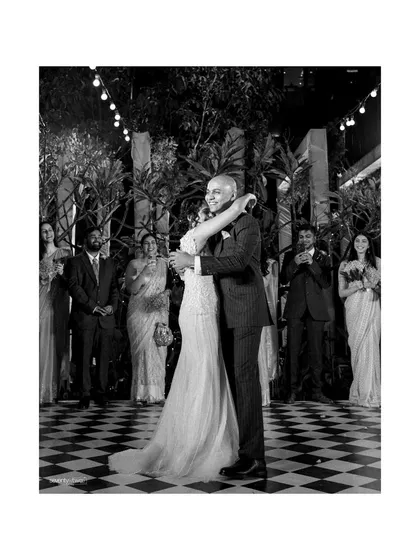 The first dance as husband and wife. This black and white photo captures the joy and emotion of the couple, surrounded by their smiling family and friends.