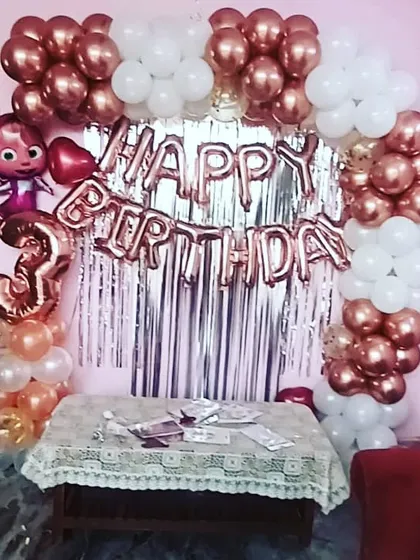 A cute Cocomelon-themed third birthday party at home. The setup includes a rose gold and white balloon arch over a silver shimmer curtain, perfect for a compact space.