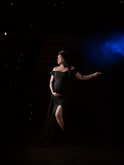 A dramatic and moody shot using creative lighting. The mom-to-be, in a classic black gown, is highlighted against a dark background, creating a powerful and artistic portrait.