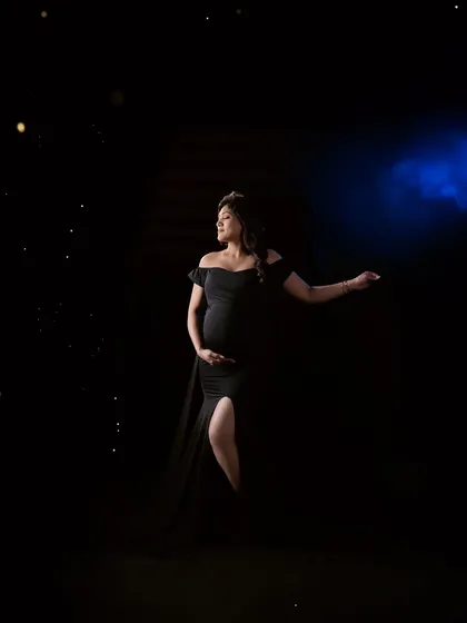 A dramatic and moody shot using creative lighting. The mom-to-be, in a classic black gown, is highlighted against a dark background, creating a powerful and artistic portrait.