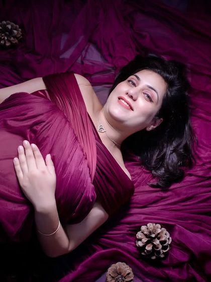 A serene, artistic shot from above. The mom-to-be lies on a bed of the same magenta fabric, creating a dreamy and ethereal portrait that focuses on her peaceful expression.
