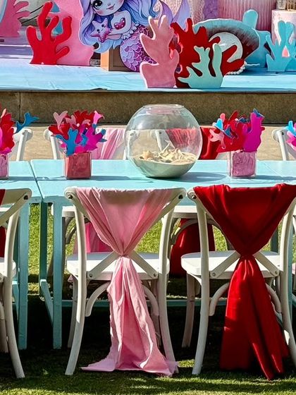 Themed table settings with coral centerpieces and chairs decorated with flowing red and pink sashes.