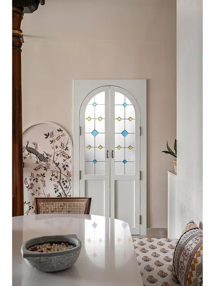 This shot highlights the beautiful stained glass kitchen door, which becomes a decorative element in the dining space. The traditional wallpaper and wooden pillar complete the modern-traditional aesthetic.