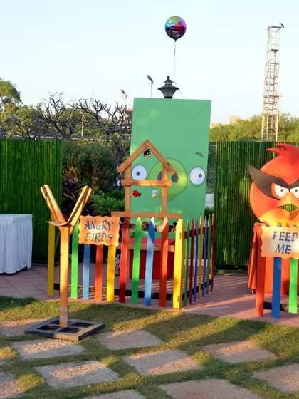 An outdoor Angry Birds party setup with interactive game stations like a life-sized slingshot and a "Feed Me" bird prop.