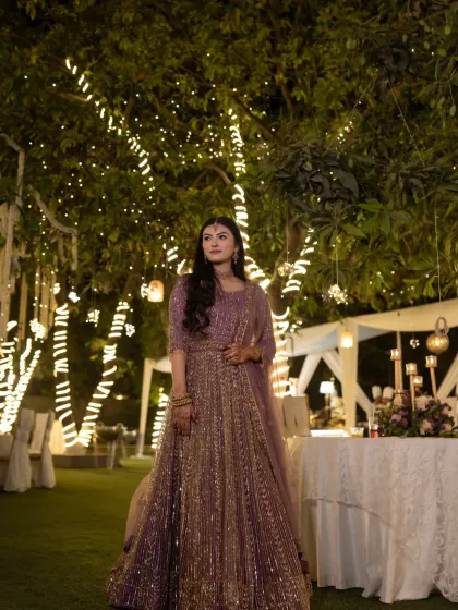 A bride standing under a canopy of fairy lights. This portrait captures the magical ambiance of an evening celebration and the elegance of her shimmering lavender lehenga.