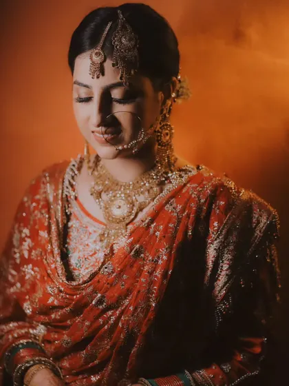 An artistic portrait of a bride captured in a moment of quiet reflection. The warm, diffused lighting creates a soft and painterly effect, highlighting her traditional jewelry.