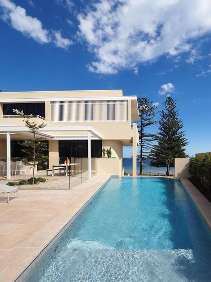 A complete view of the pool and patio area at a coastal property. The design is clean and bright, using light-colored paving and simple lines to reflect the beachside environment.