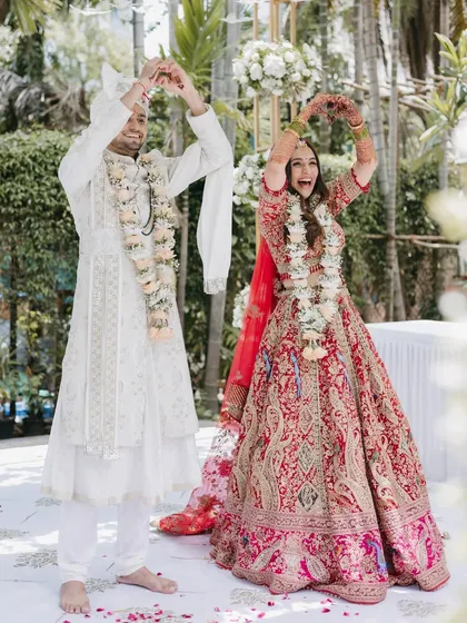 The couple shares a fun, choreographed pose during their ceremony, making hearts with their hands, reflecting their playful and happy personalities.