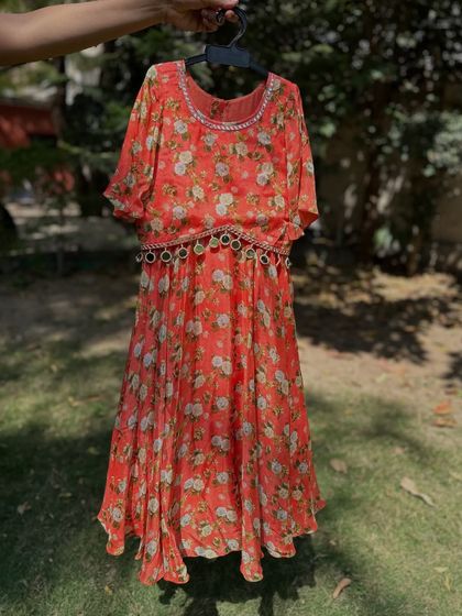 This orange floral dress is another beautiful option for summer events. The pleated skirt and mirror-work belt add a touch of sophistication, while the bright color keeps it fun and youthful.