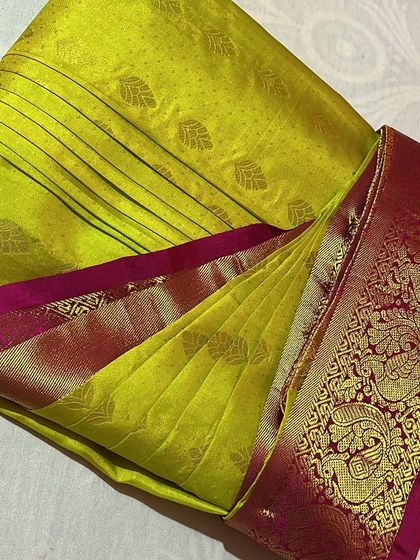 A vibrant lime green silk saree with a rich pink border, expertly pleated and ready for a celebration. The pleats are set to highlight the beautiful border design.