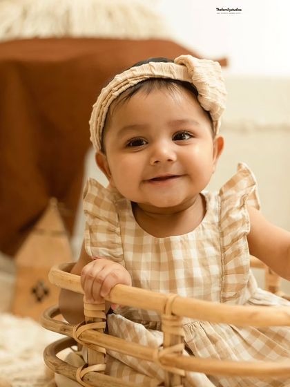 A sweet and simple portrait of a baby girl in a gingham dress, capturing her calm and happy demeanor.